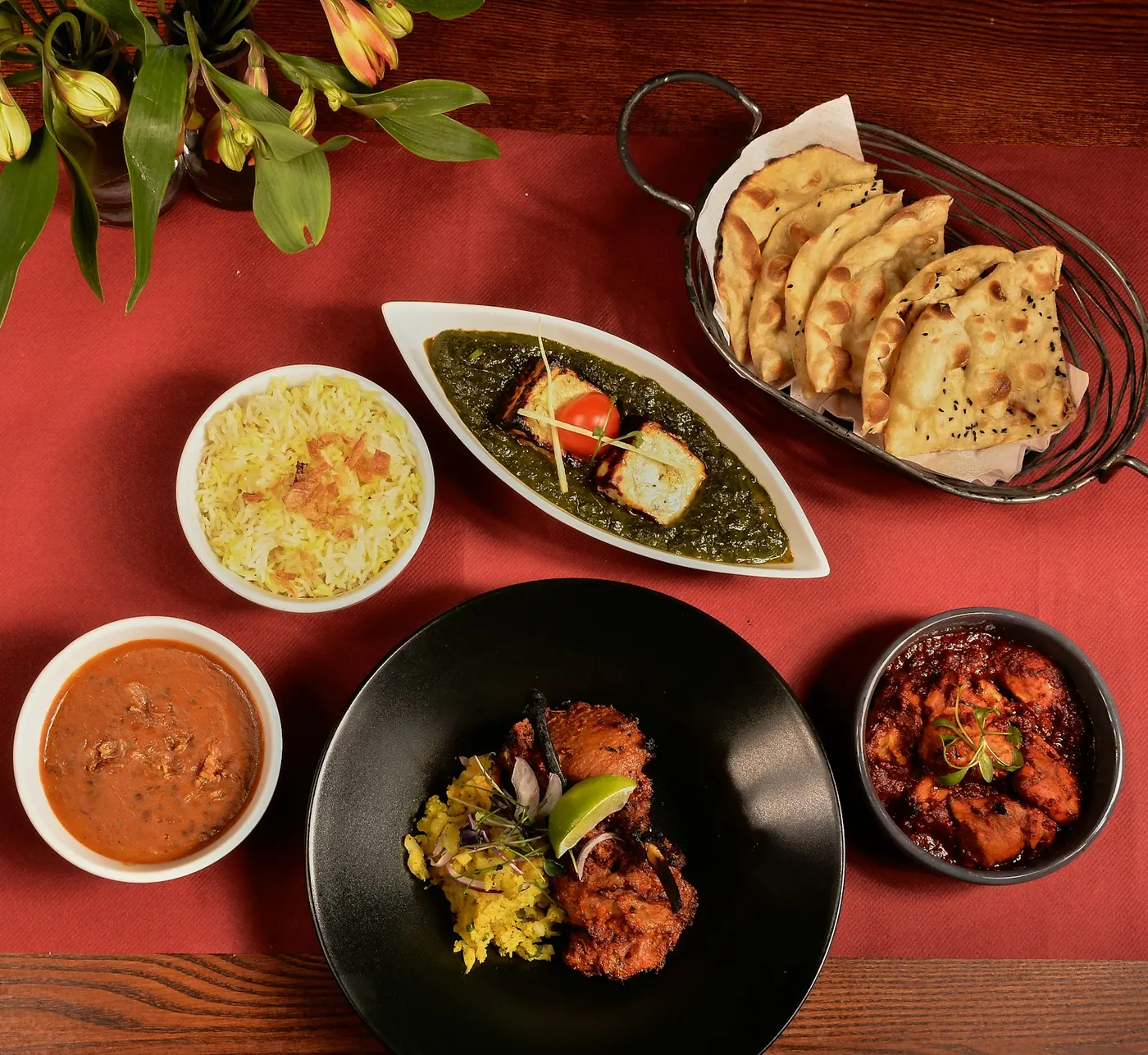 Indian curries, rice, paneer and flatbreads arranged across a red table